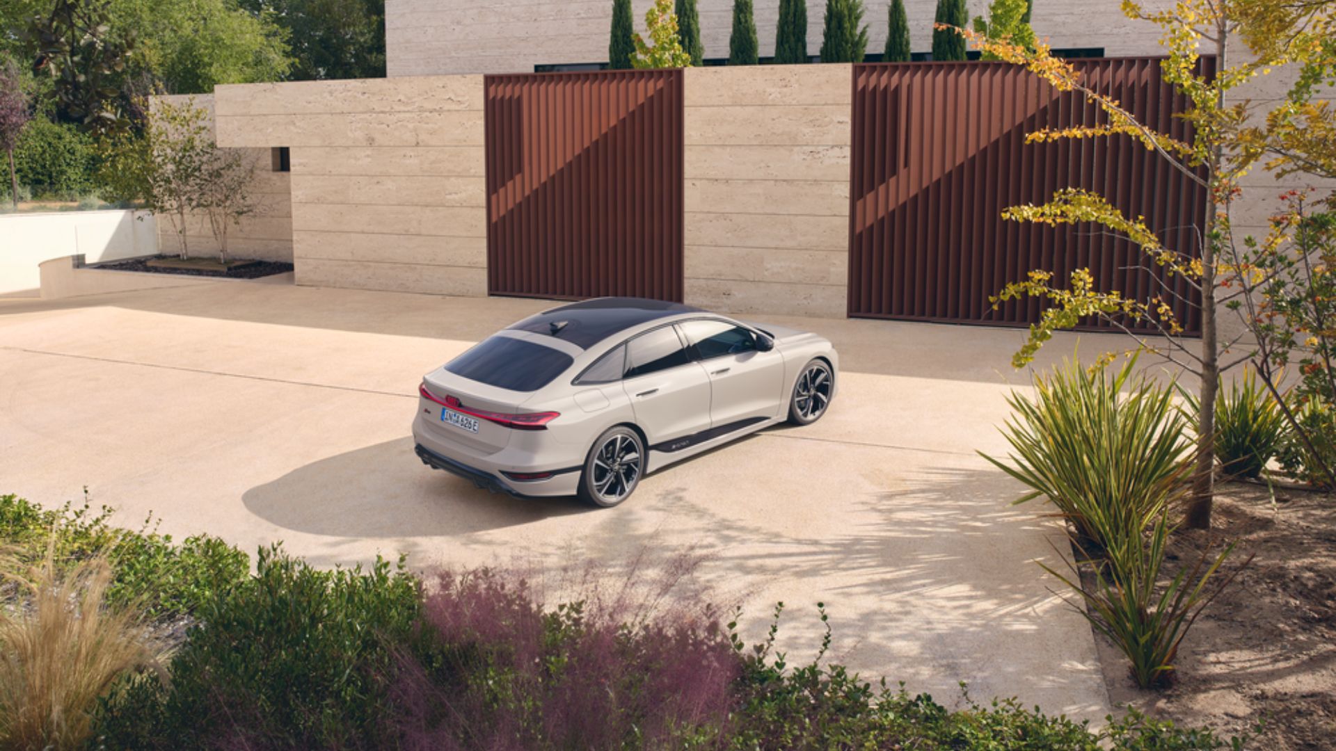 Audi a6 e-tron parkerad på uppfat med ljusasfalt, omgivet av grönskande gräsmatta och buskar.